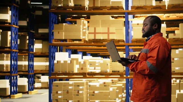 Portrait of african american worker using laptop for inventory management. Fulfillment center operations coordinate shipping and delivery, maintaining efficient supply chain workflow performance.