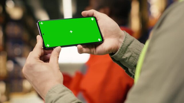 Chroma key on phone, with employee near racks, cardboard boxes in busy depot. Supply chain operations and inventory management creates import export and e-commerce industry, dispatch.