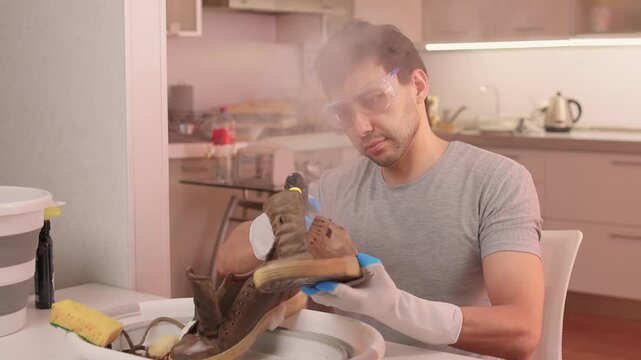 Man steam cleans rugged footwear carefully. Person uses steam to restore sturdy shoes meticulously. Individual refurbishes tough leather shoes with focused steam technique