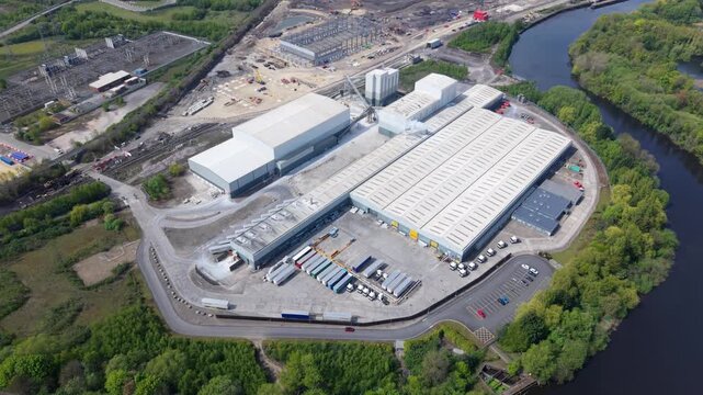 Aerial view of Ferrybridge industrial facility with large warehouses, parked trucks, and a river in Knottingley, England, United Kingdom.