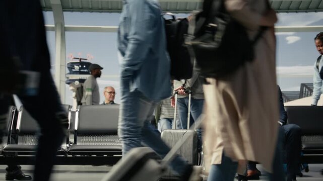 Passengers carrying trolleys in airport transport hub overlooked by runway control tower. Diverse travelers walking with luggage inside flight departure terminal, camera A