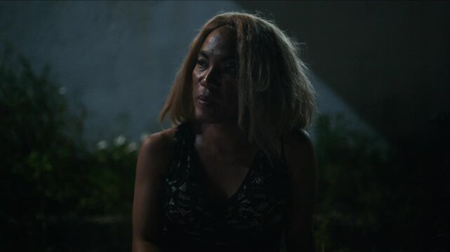 Sad and tired transgender woman with messy hair smoking a cigarette alone in a dark environment
