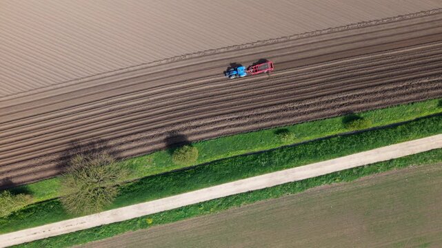 Aerial view of a blue tractor with a red trailer plowing a furrowed field near Ferrybridge Knottingley, England, United Kingdom.