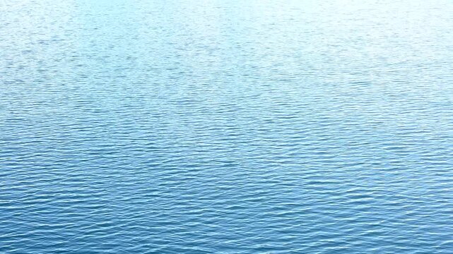 4K HD video flying above calm rippling blue water.
