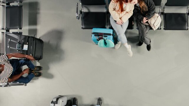 Top down view of passengers in airport scrolling on smartphones during flight layover, traveling by plane. Travelers waiting for boarding, using phone to access online flight schedule, high angle shot