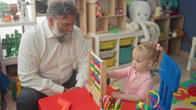 Man watches little girl move colored beads on wooden abacus at play table in building; tender bonding.