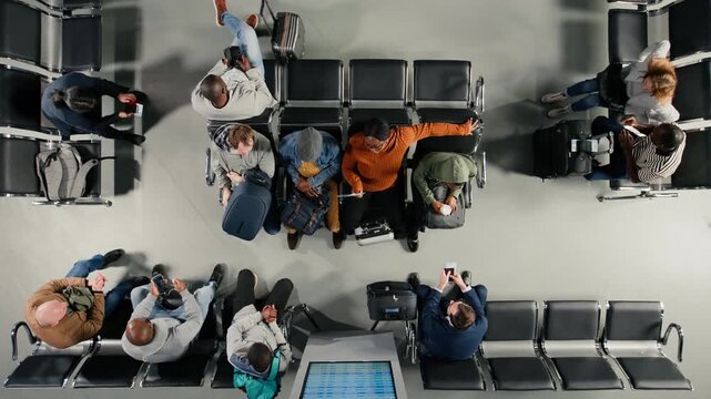 Group of passengers in airport terminal checking departure board for timetable, top down view. Multiethnic tourists looking at FIDS screen schedule, catching plane for holiday trips, high angle shot
