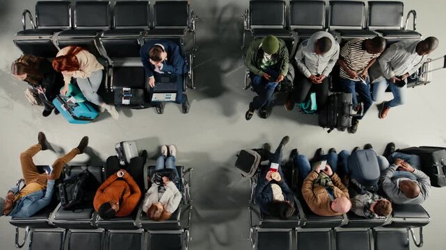 Tourists in airport lounge boarding for departing airplane flights, standing up from chairs, going to aircraft bridge. Passengers leaving airport terminal, going to boarding gate with trolleys