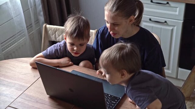 Mother teaches sons joyful togetherness. Mother and sons engage happily during learning time at home. Nurturing mother and her two sons enjoy fun learning session around kitchen table