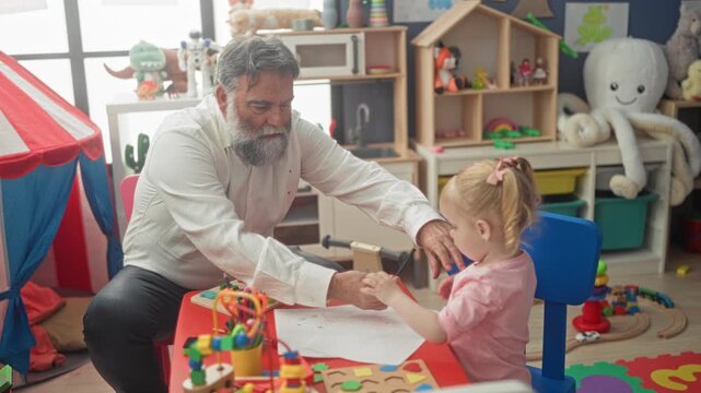 Man hands yellow pencil to toddler at playroom table in building while guiding drawing and sharing tools; tenderness early learning.