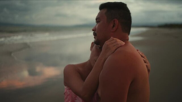 Affectionate transgender woman embracing her boyfriend from behind on a cloudy evening at the beach