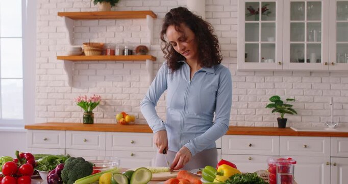 Positive woman cooking healthy vegetarian vegetable salad by chopping on kitchen counter at home, focusing on food preparation in a personal setting with care and culinary engagement.