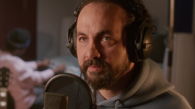 Professional male singer in headphones performing into condenser microphone while recording vocals in music studio. Close up view