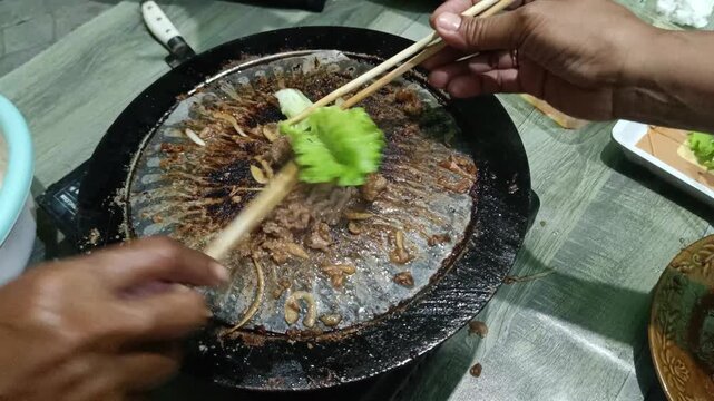 Cooking Beef and Lettuce on a Hot Round Grill with Chopsticks