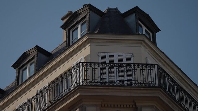 Exterior establishing shot of a classic Parisian building featuring a balcony with ironwork and closed shutters The architecture is typical of Paris France showcasing a romantic and historical city lo