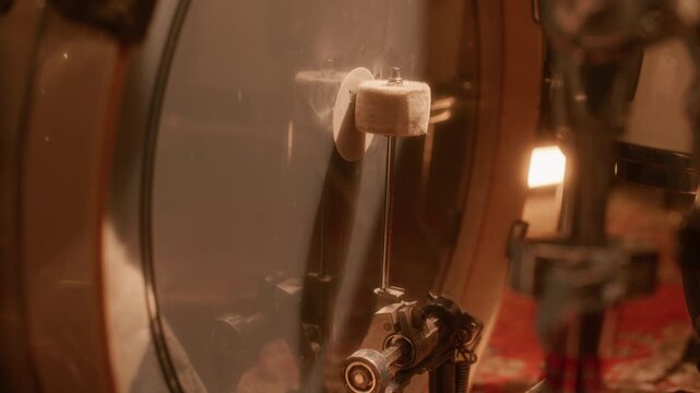 Close up view of striking bass drum beater during music recording session or rehearsal in warmly lit studio