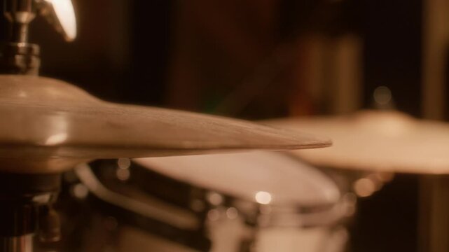Close up view of drumstick hitting cymbal during energetic drum performance or rehearsal in music studio illuminated by warm light
