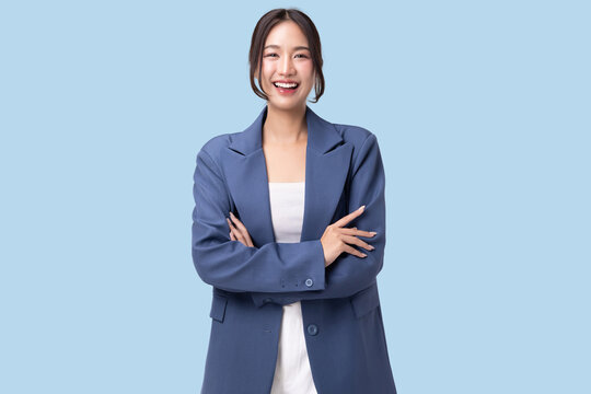Portrait of a confident young Asian businesswoman in blue blazer smiling and looking at camera. Happy female entrepreneur with arms crossed posing against light blue background, smart and professional
