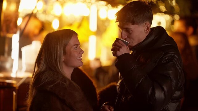 A romantic couple in Paris France at a Christmas market The man and woman are in love talking and drinking a hot beverage at night during winter The shot is handheld capturing the intimate moment betw