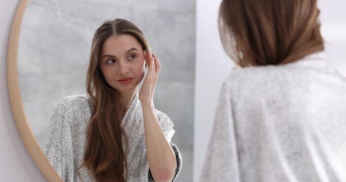 Beautiful young woman doing facial self massage near mirror indoors, selective focus