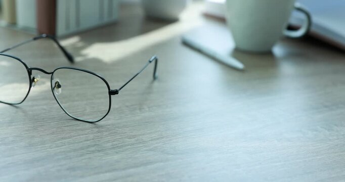 Stylish glasses, stationery and coffee on wooden table indoors, closeup. Camera moving right