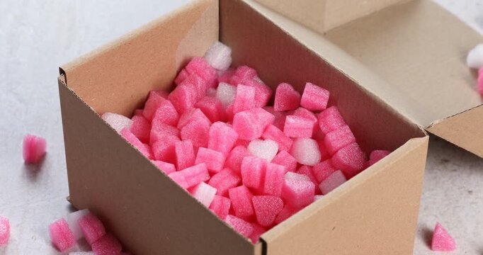 Woman putting styrofoam pieces into cardboard box at light grey table, closeup