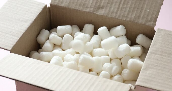 Styrofoam pieces falling into cardboard box on pink table, closeup