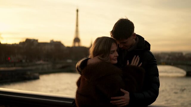 A romantic couple embraces with the Eiffel Tower visible in the background during sunset in Paris France The River Seine flows in the foreground Golden hour light bathes the scene.