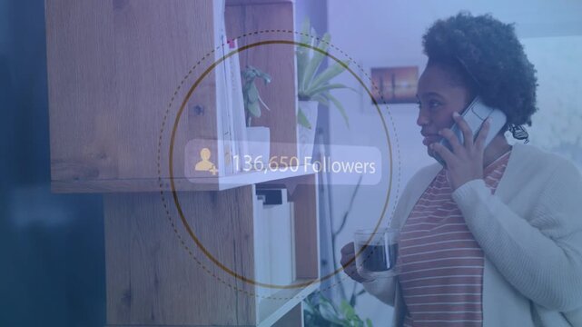 Woman by shelf, on phone holding mug watching follower overlay appearing and tracking social growth