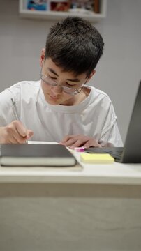 Clever scholar studying with laptop and writing notes in notebook at desk. Vertical reels of real people, authentic remote education and modern education concept.