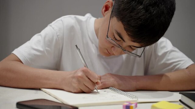 Concentrated pupil writing notes in notebook during study session at home. Real people, authentic education, learning and productivity concept.