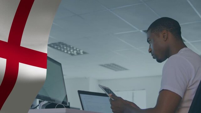 Man holding tablet and comparing monitors in tech office, red-cross flag waving, verifying data