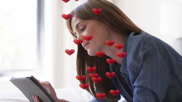 Woman tapping tablet while reclining by window, causing red hearts occluding face for social app