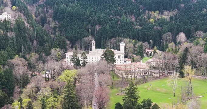 Aerial view of the historic Vallombrosa Abbey complex surrounded by dense evergreen forests and a green meadow in the Apennine Mountains Vallombrosa, Tuscany, Italy.