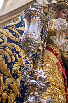 Ornate processional candle holder with angel figure beside Virgin Mary sculpture, highlighting Catholic symbolism and ceremonial devotion in religious tradition