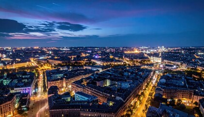Fototapeta premium Aerial cityscape at dusk with illuminated buildings and roads, under a dramatic, colorful sky