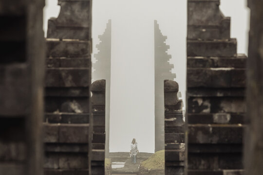 View of Cetho Temple with its iconic split stone gateway shrouded in mist and a person walking through the ancient Hindu site Kecamatan Jenawi, Jawa Tengah, Indonesia.