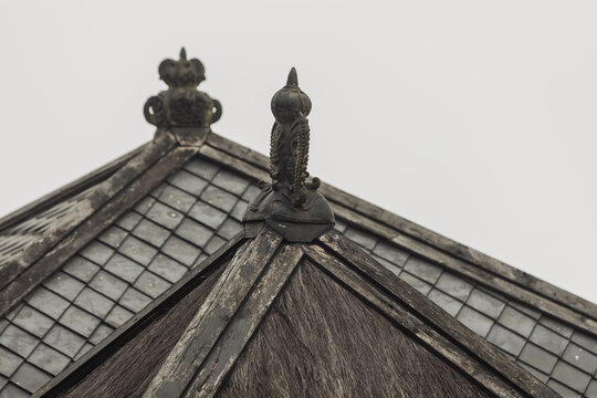 View of the ornate roof finials and weathered shingles of Cetho Temple under an overcast sky in Kecamatan Jenawi, Jawa Tengah, Indonesia.