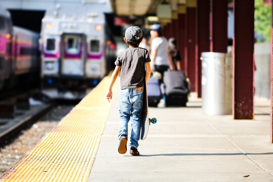 Rear view of a young boy carrying a skateboard on a train station platform in Boston during a family road trip across America.