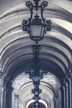 View of the ornate iron lanterns hanging from the vaulted stone arches of the arcade at Praca do Comercio Lisbon, Lisbon, Portugal.