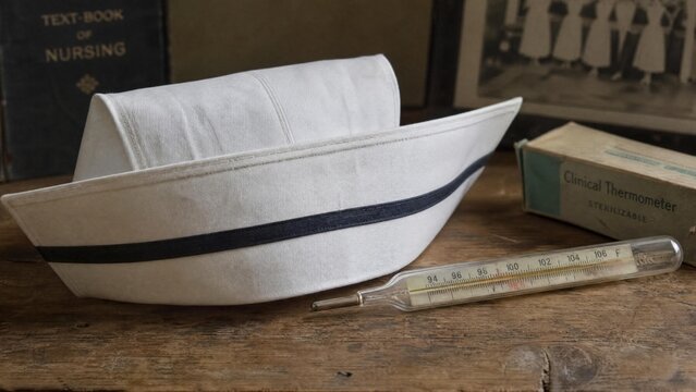 Vintage Nursing Memorabilia with Classic White Nurse Cap and Glass Clinical Thermometer on Wooden Surface