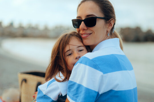 Happy Mother and Daughter in Matching Striped Shirts Hugging. Smiling mom wearing sunglasses embracing her little girl during a seaside vacation.
