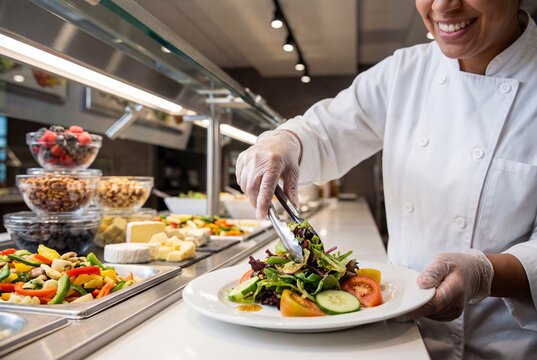 Professional chef serving a fresh green salad from a buffet line in a commercial kitchen or cafeteria