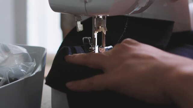 Close-up of woman's hands sewing navy blue fabric with a professional sewing machine.