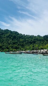 Sea gypsies wooden frishing boat on turquoise water n calm ocean wave at Moken or Morgan Village in Surin island with mountain n rain-forest in tropical summer sunlight on clear blue sky n white cloud