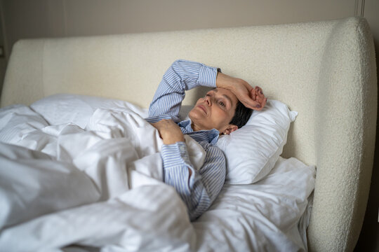 Unhappy thoughtful senior woman lying in bed in morning at home with lost exhausted expression, elderly female in bedroom showing loneliness and depression at older age, life crisis and mental issues.