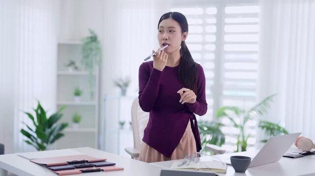 Asian women beauty influencer applying lipstick makeup tutorial recording video content for social media vlog at home office desk with laptop bright modern
