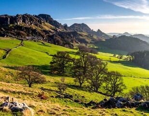 Obraz premium Scenic Green Rolling Hills And Rocky Mountain Peaks Under Bright Blue With Warm Golden Sunlight Casting Long Shadows Over The Rural Landscape