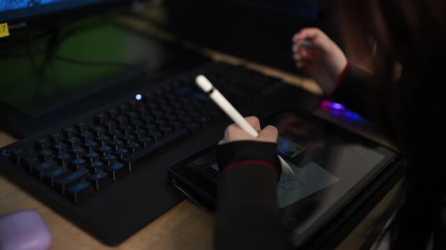 Digital artist drawing on tablet computer with stylus, computer keyboard and monitor.