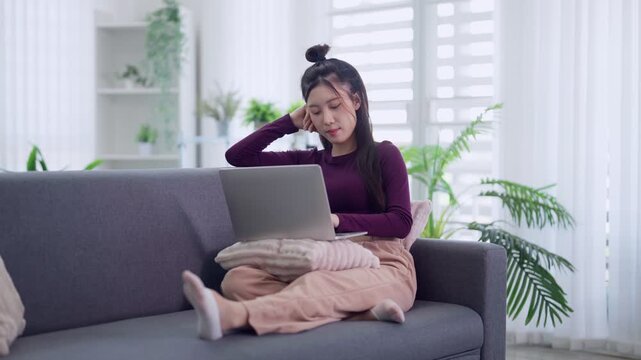 stressed Asian women working from home using laptop computer sitting on sofa feeling tired confused worried about problem remote work freelancer struggle with